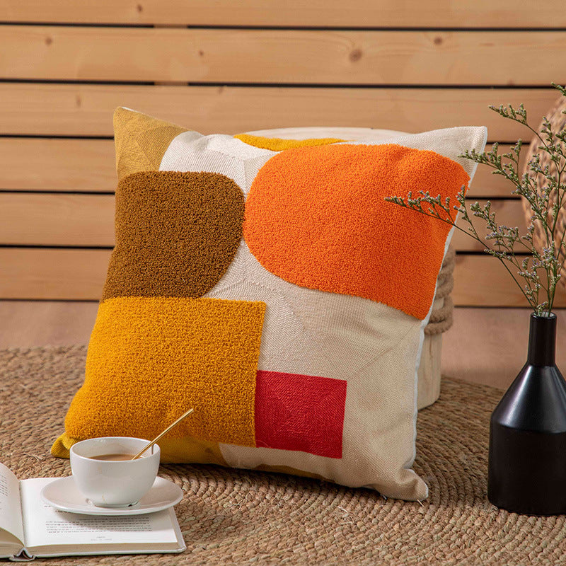 Colorful geometric pillow on a wooden surface with a cup of coffee and a vase.