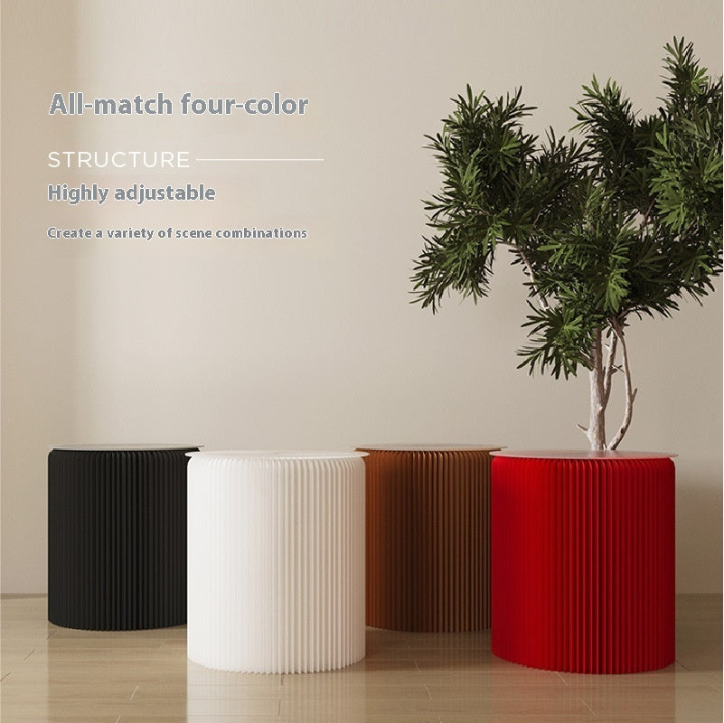 Four cylindrical stools in black, white, brown, and red with a plant on a beige background.