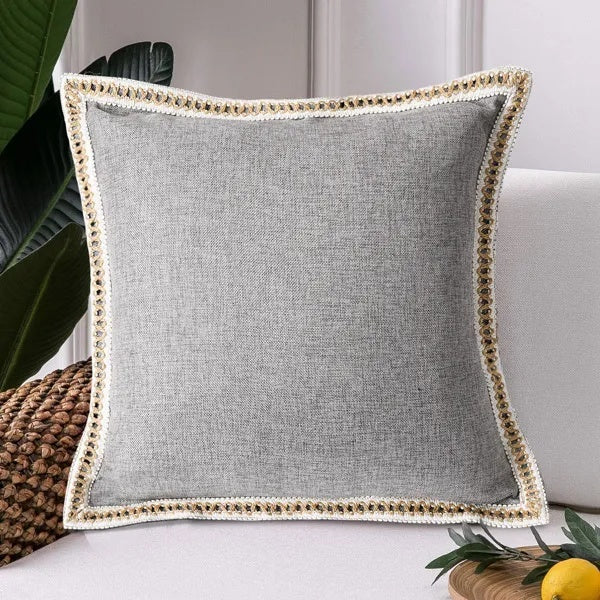 Gray pillow with decorative trim on a white surface
