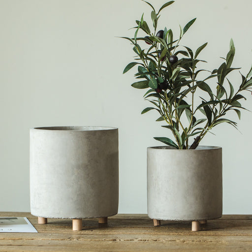 Two concrete planters with a plant on a wooden surface against a light background