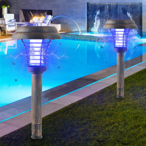 Two solar-powered garden lights by a pool with a fireplace and water feature in the background.