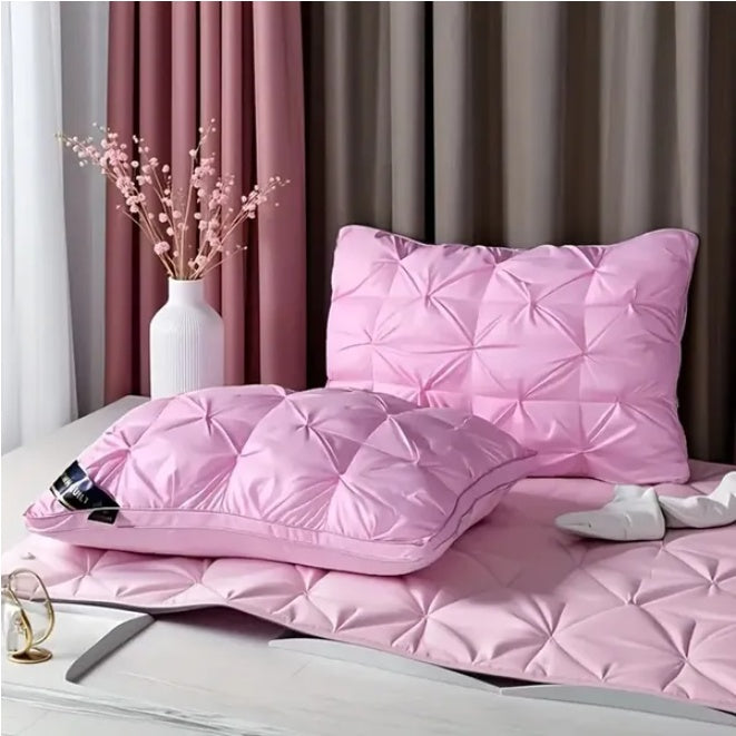 Pink quilted comforter and pillow on a bed with pink curtains in the background.