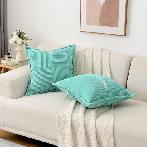 Two turquoise pillows on a beige sofa with a decorative plant and framed art in the background.